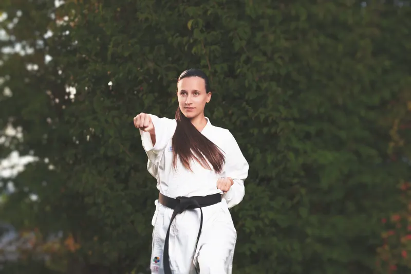 Karateka in weißem Karate-Gi mit Schwarzgurt bei einer Schlagtechnik im Freien