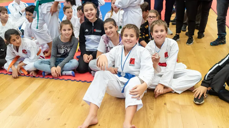Gruppe Kinder im Karategi sitzt lächelnd auf dem Boden