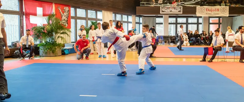 Kind tritt mit erhobenem Bein gegen Gegner auf der Matte