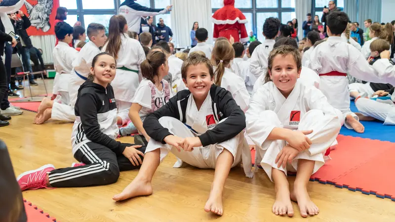 Drei Kinder sitzen lachend auf dem Hallenboden