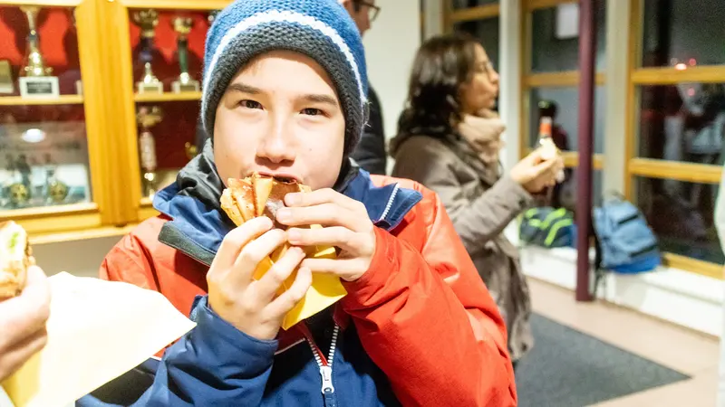Kind isst ein Brot im Freien, Person im Hintergrund