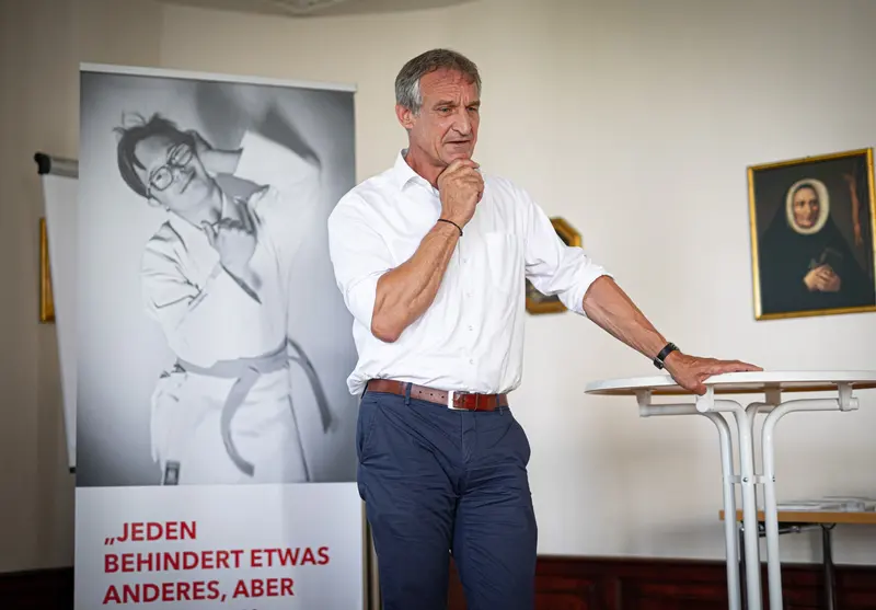 Person steht neben einem Plakat und spricht gestikulierend.
