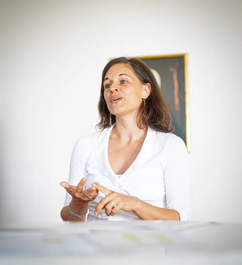 Person spricht gestikulierend vor Porträtbildern an der Wand.