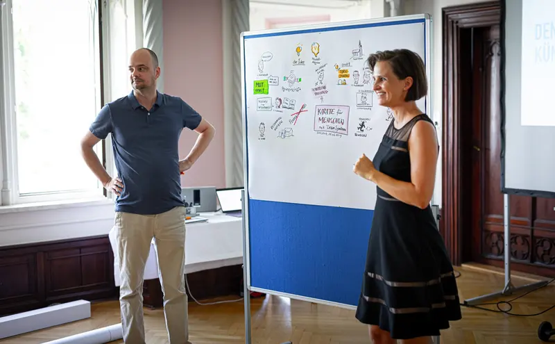 Person steht neben Flipchart mit Sketchnotes, andere daneben.