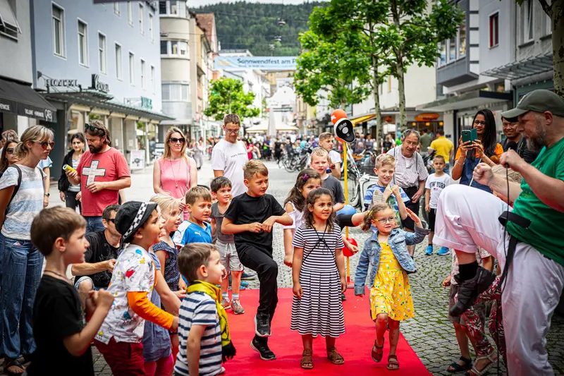 Blick auf belebte Fußgängerzone mit Kindergruppe und Publikum