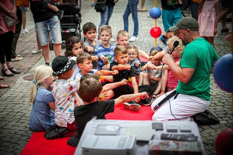 Kinder drängen sich um eine Person unter bunten Luftballons