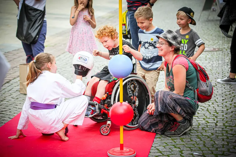 Person kniet bei einem Kind im Rollstuhl, daneben ein Kind in Karategi
