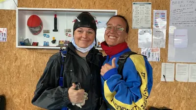 Zwei Personen in Fallschirmspringer-Ausrüstung zeigen den Daumen hoch