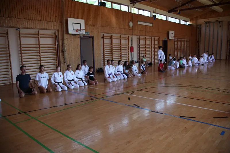 Gruppe sitzt an der Wand einer Sporthalle