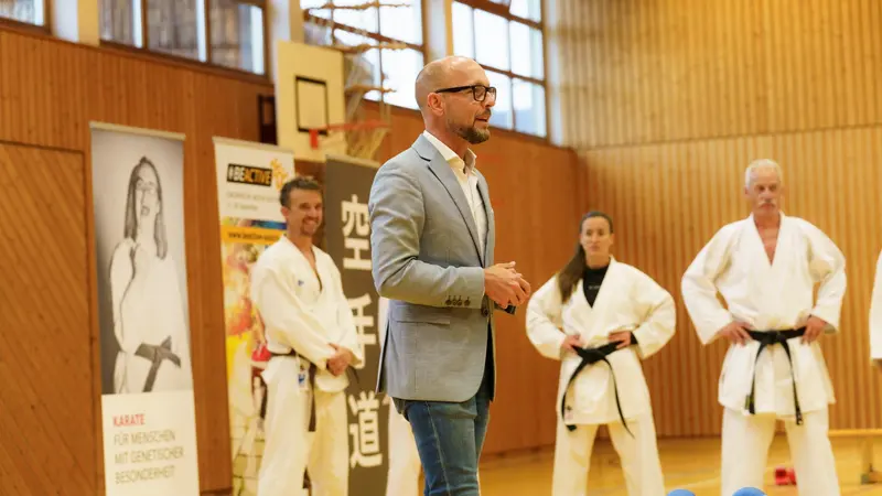 Person hält Ansprache vor Karategruppe in der Halle