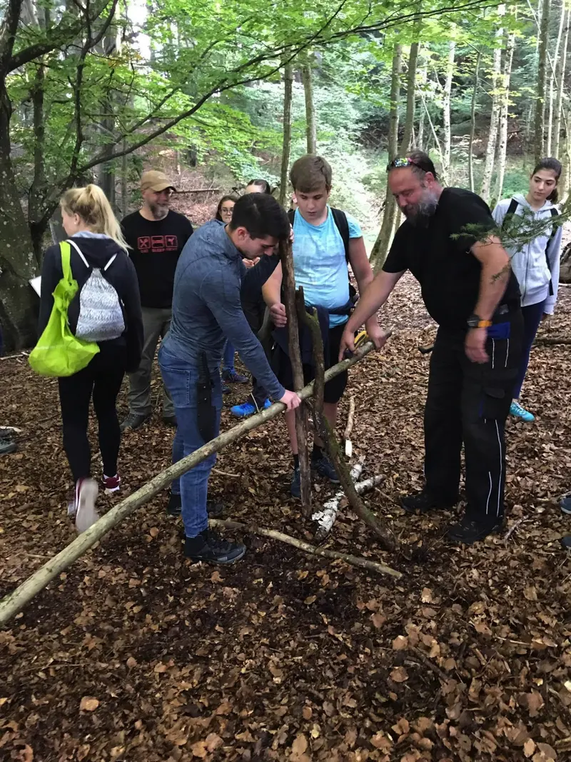Person blickt lächelnd aus fertigem Unterschlupf im Wald