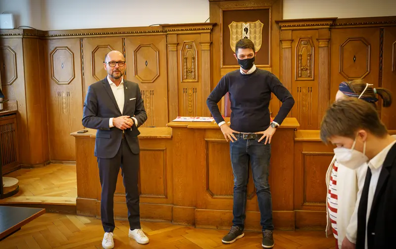 Zwei Personen stehen nebeneinander in einem holzgetäfelten Saal