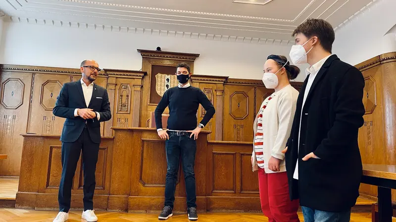 Vier Personen stehen nebeneinander im holzgetäfelten Saal