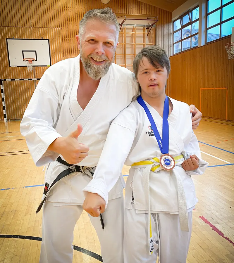 Trainer und Sportler mit Medaille umarmen sich lachend