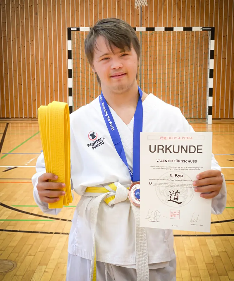 Jugendlicher mit Medaille hält Urkunde und Gürtel hoch
