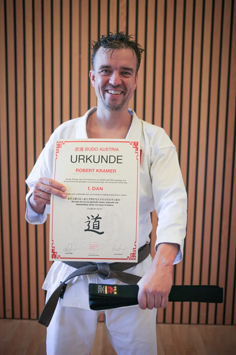 Person im Karategi hält lächelnd Urkunde mit Aufschrift '1. Dan'