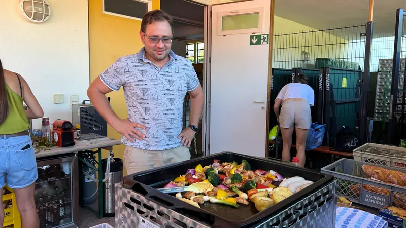 Person steht lächelnd neben Grill mit buntem Gemüse im Freien