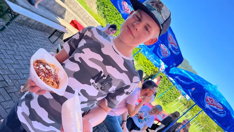 Person in gemustertem Shirt hält Teller mit Pizzastück im Freien