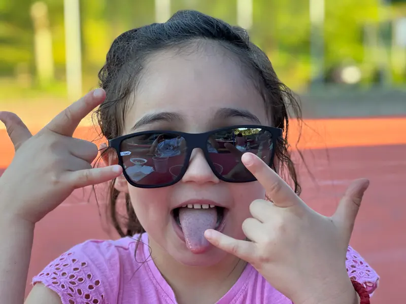 Kind mit Sonnenbrille streckt lachend die Zunge heraus