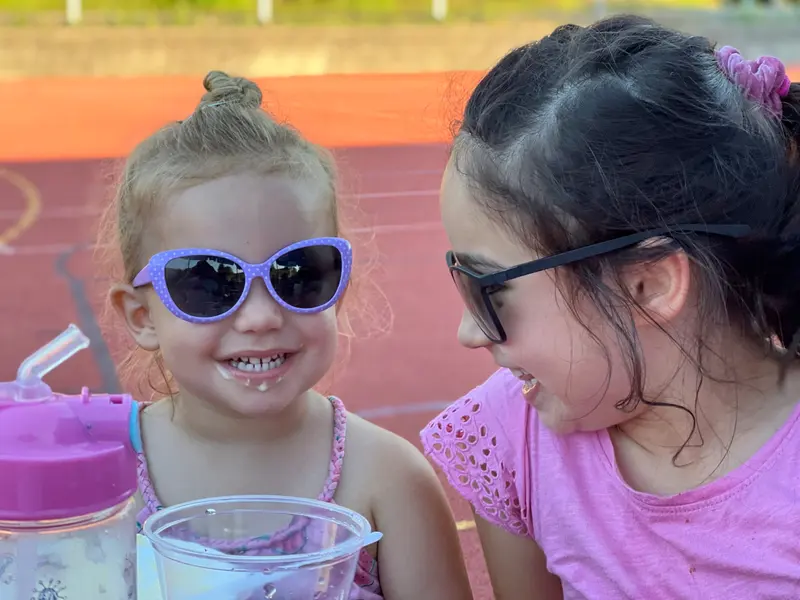 Zwei Kinder mit Sonnenbrillen sitzen lachend nebeneinander im Freien