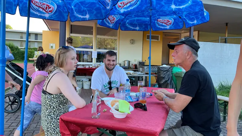 Personen sitzen gemeinsam an gedecktem Tisch unter Sonnenschirm im Freien