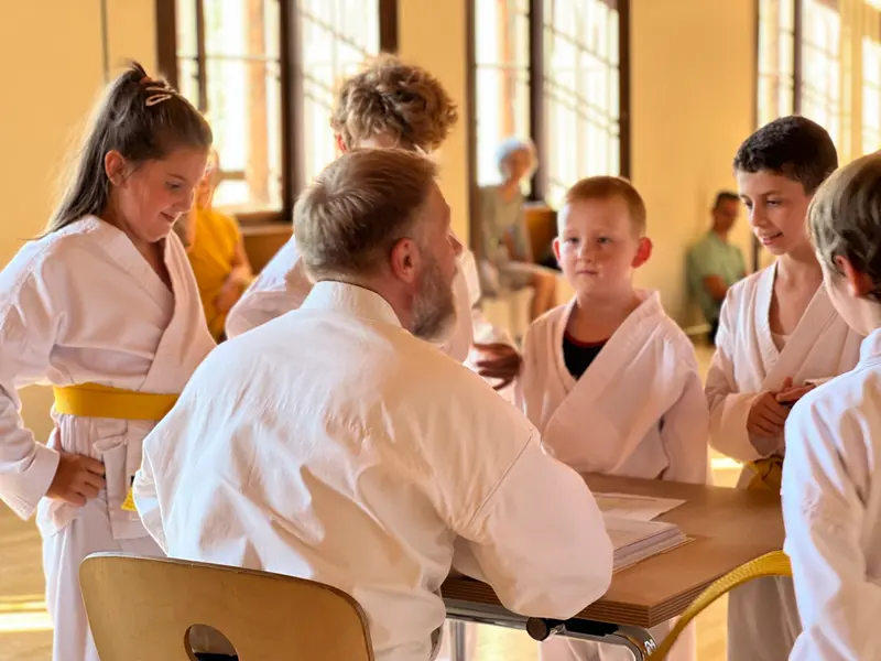 Prüfer sitzt am Tisch mit Kindern im Gespräch