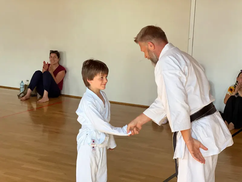 Kind schüttelt Prüfer mit schwarzem Gürtel die Hand