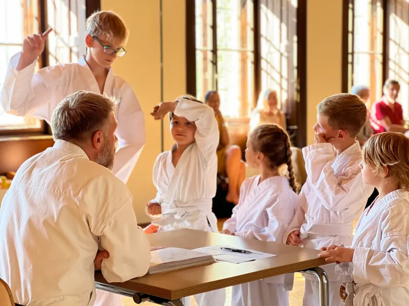Prüfer sitzt am Tisch, Kinder stehen daneben