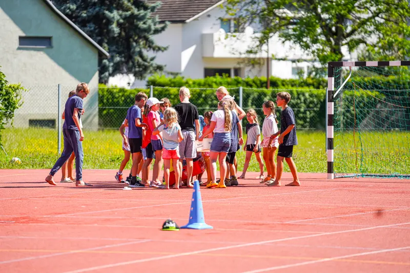 Kinder spielen gemeinsam mit Trainer auf Sportplatz im Freien