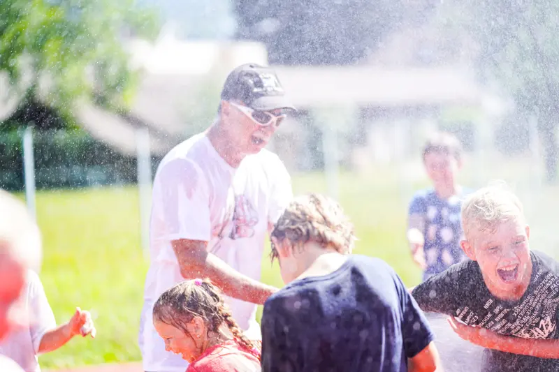 Trainer bespritzt lachende Kinder mit Wasser im Freien