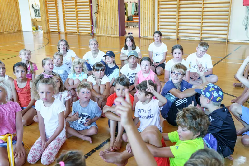 Gruppe Kinder sitzt dicht gedrängt auf dem Hallenboden