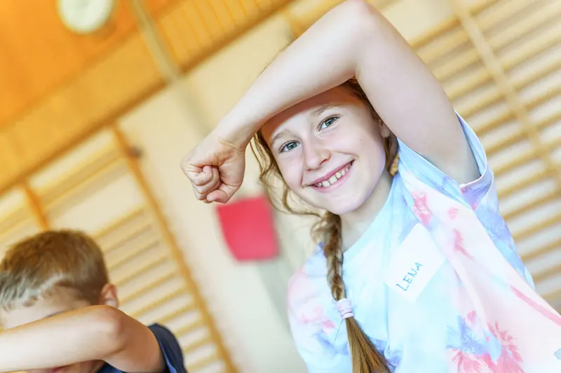 Kind im Freien hält lächelnd den Arm schützend über die Augen