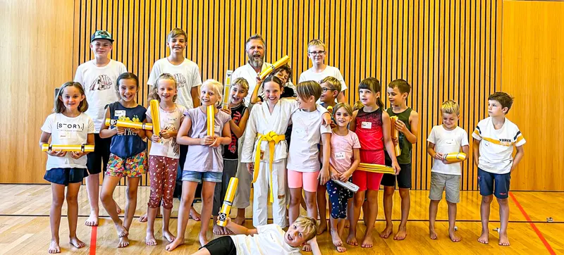 Gruppe aus Kindern und Erwachsenen posiert in der Turnhalle mit gelben Bändern