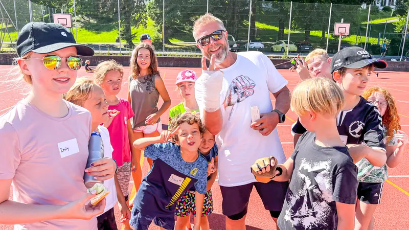 Gruppe aus Kindern und Erwachsenem steht lachend zusammen im Freien