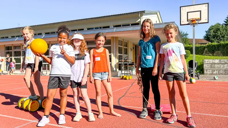 Kinder mit orangem Ball stehen auf Sportplatz im Freien