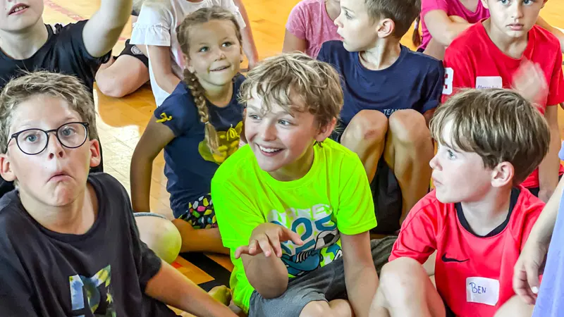 Gruppe Kinder sitzt eng zusammen, ein Junge im neongrünen Shirt lacht