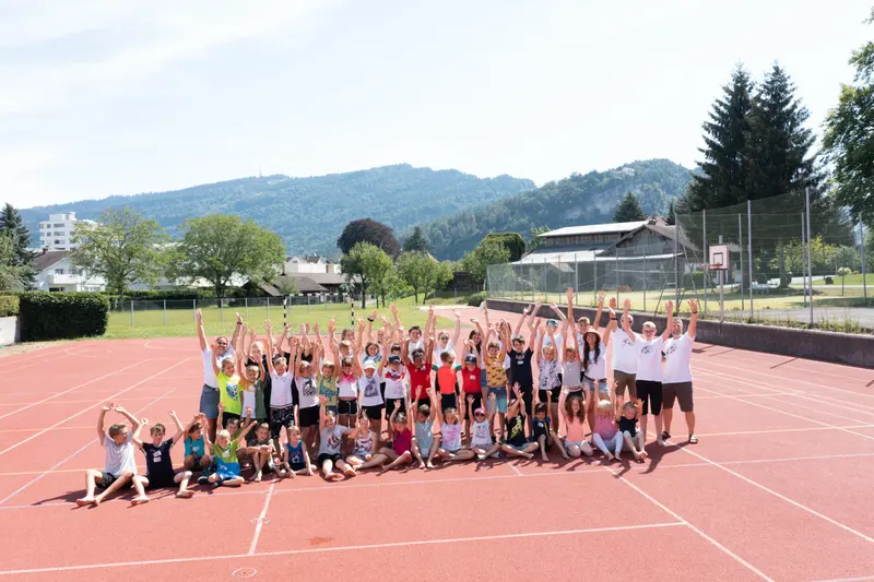 Große Kindergruppe jubelt mit erhobenen Armen auf Laufbahn im Freien