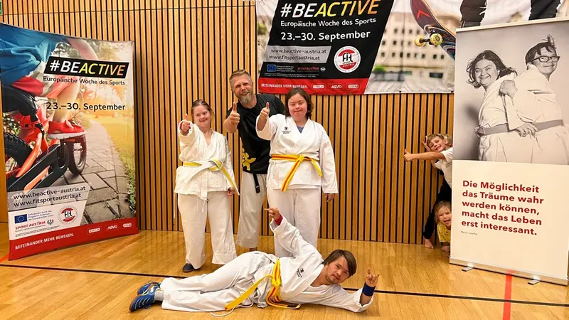 Vier Personen im Karategi posieren lachend vor #BeActive-Plakat