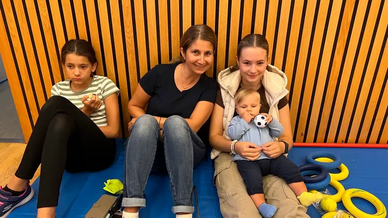 Zwei Kinder und Erwachsene sitzen lächelnd zusammen auf einer Matte