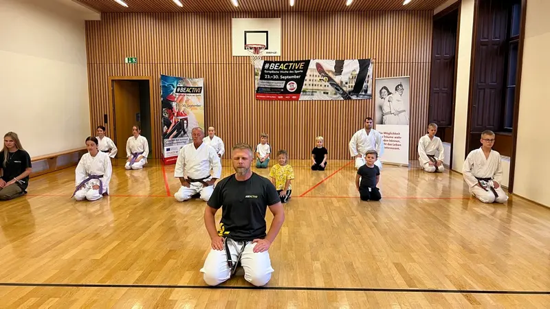 Trainer kniet mit Kindern im Karategi in der Turnhalle