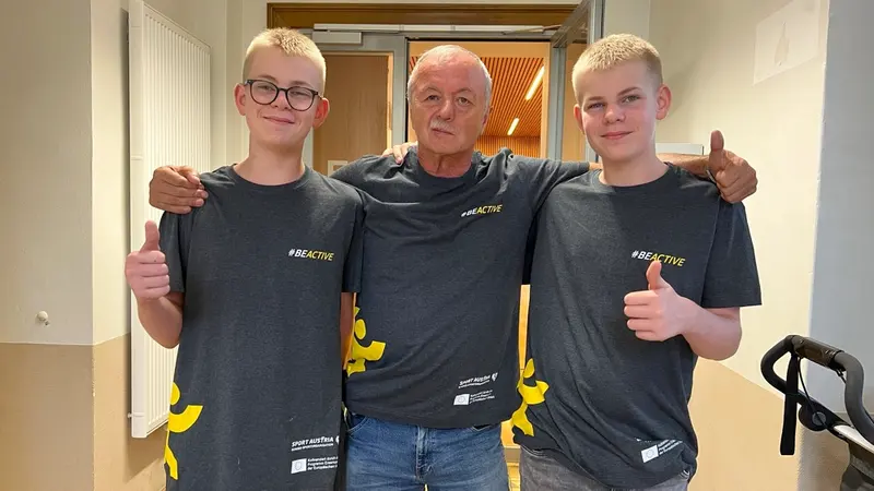 Drei Personen in #BeActive-Shirts posieren lächelnd nebeneinander