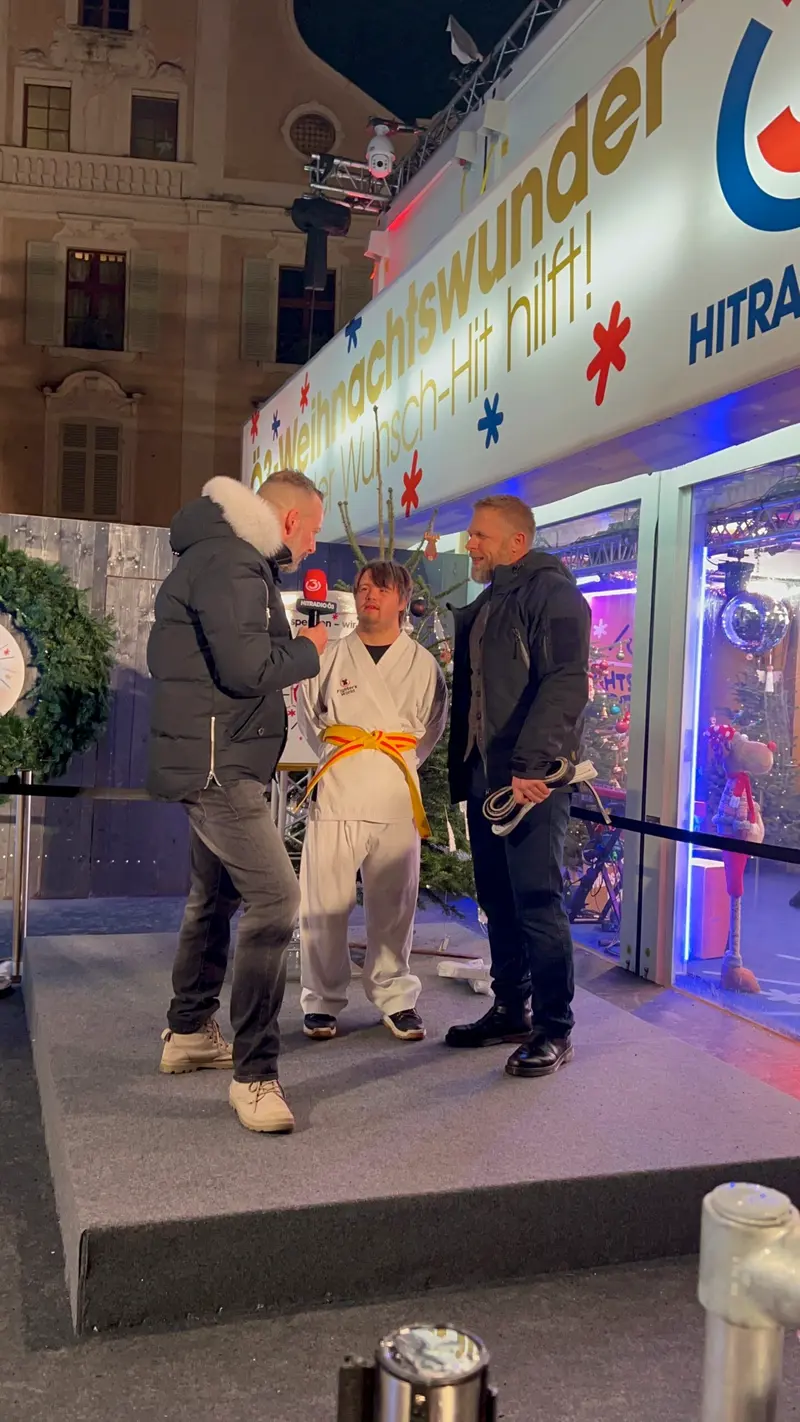 Person im Karategi mit orangem Gürtel wird von zwei Personen mit Mikrofon interviewt