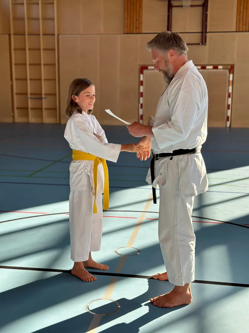 Kind mit gelbem Gürtel schüttelt dem Prüfer die Hand