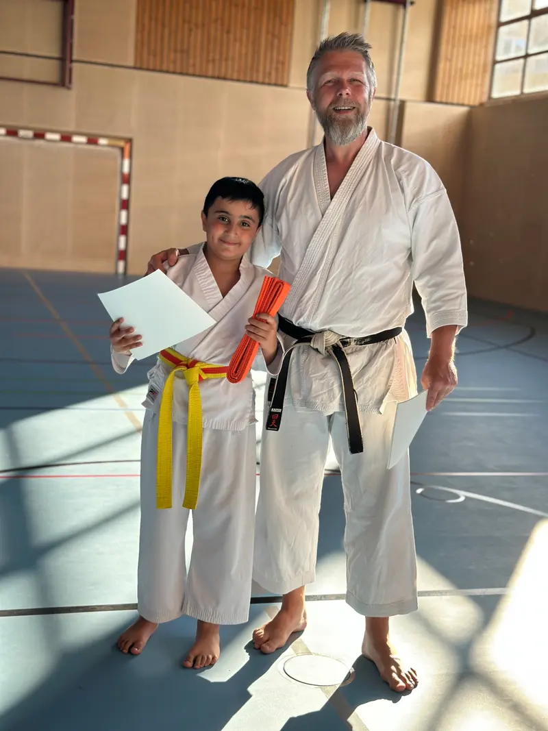 Kind mit gelbem Gürtel hält Urkunde und neuen orangen Gürtel