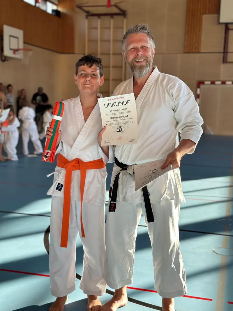 Kind mit orangem Gürtel hält Urkunde, Prüfer hält weiteres Blatt