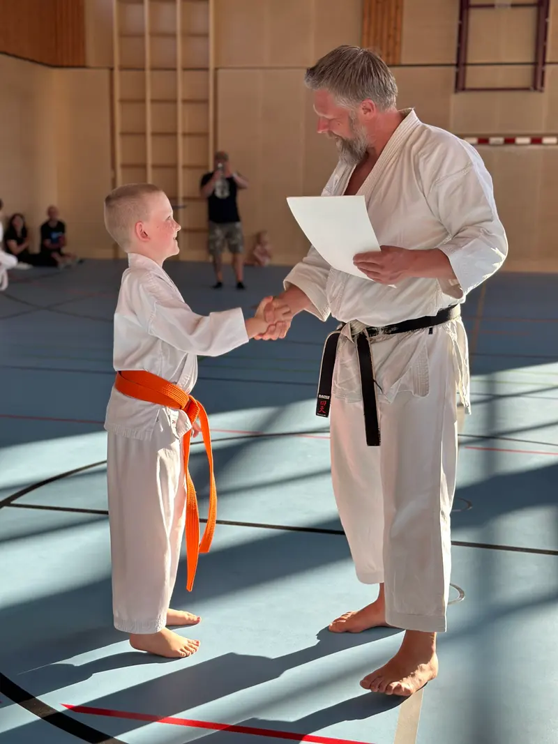 Kind mit orangem Gürtel und Prüfer reichen sich die Hand