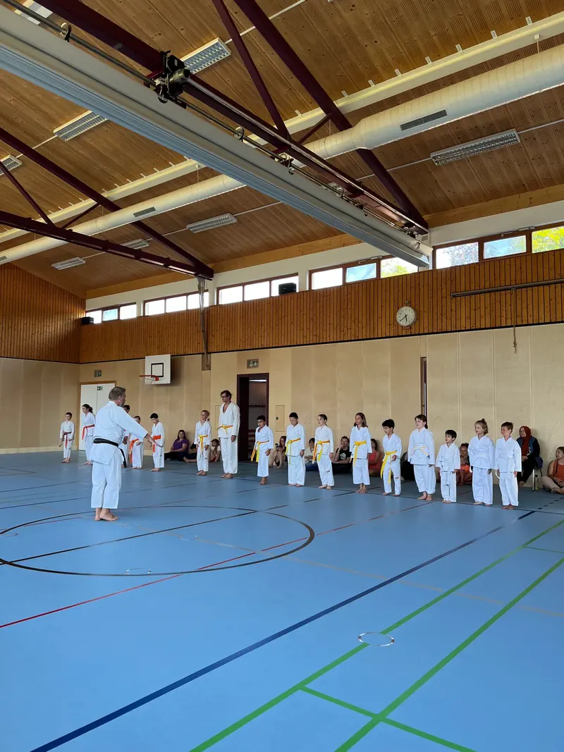 Prüfer steht vor einer aufgereihten Gruppe Kinder in der Halle