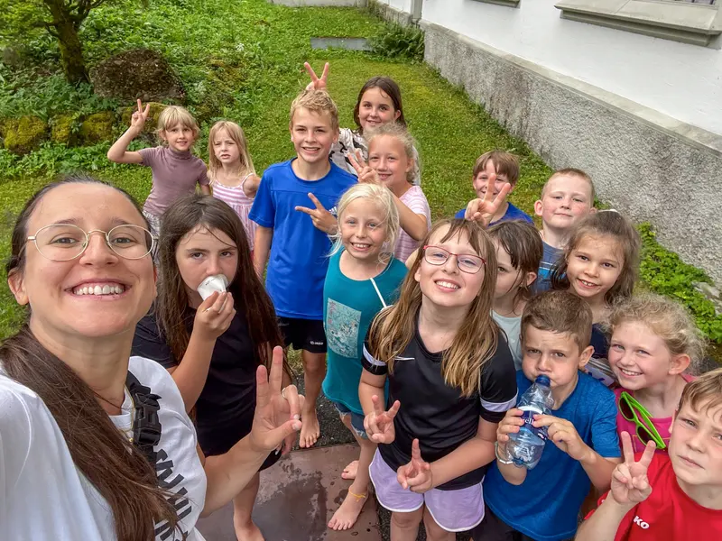 Kinder posieren mit Handzeichen für ein Gruppenfoto auf einer Wiese