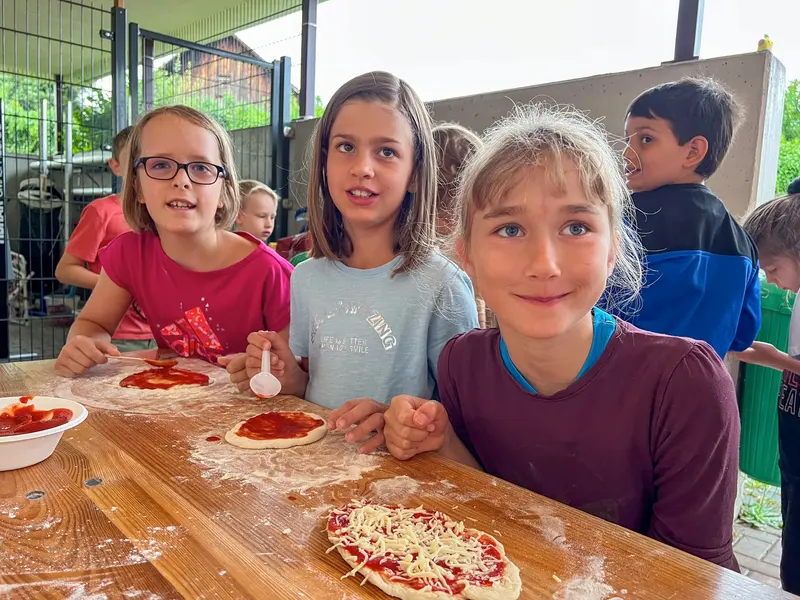 Kinder bereiten an einem Tisch im Freien Pizzateig zu