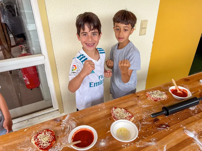 Zwei Kinder stehen an Tisch mit Pizzasoße und Schüsseln